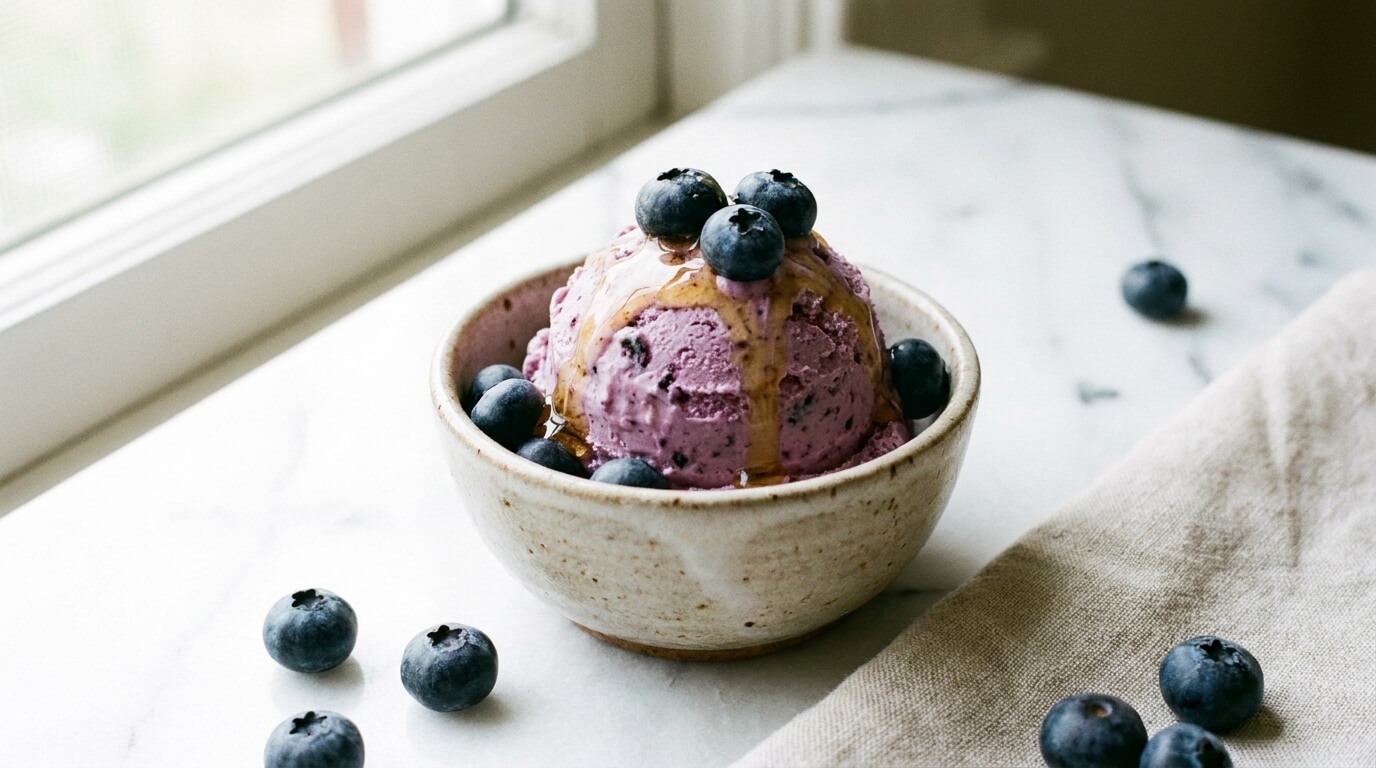 Creamy blueberry cottage cheese ice cream in a bowl topped with fresh blueberries and a honey drizzle