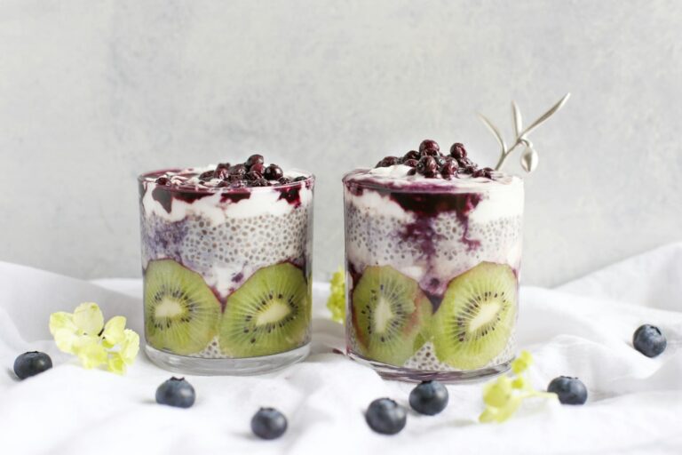 Two glasses of chia pudding layered with kiwi and blueberries