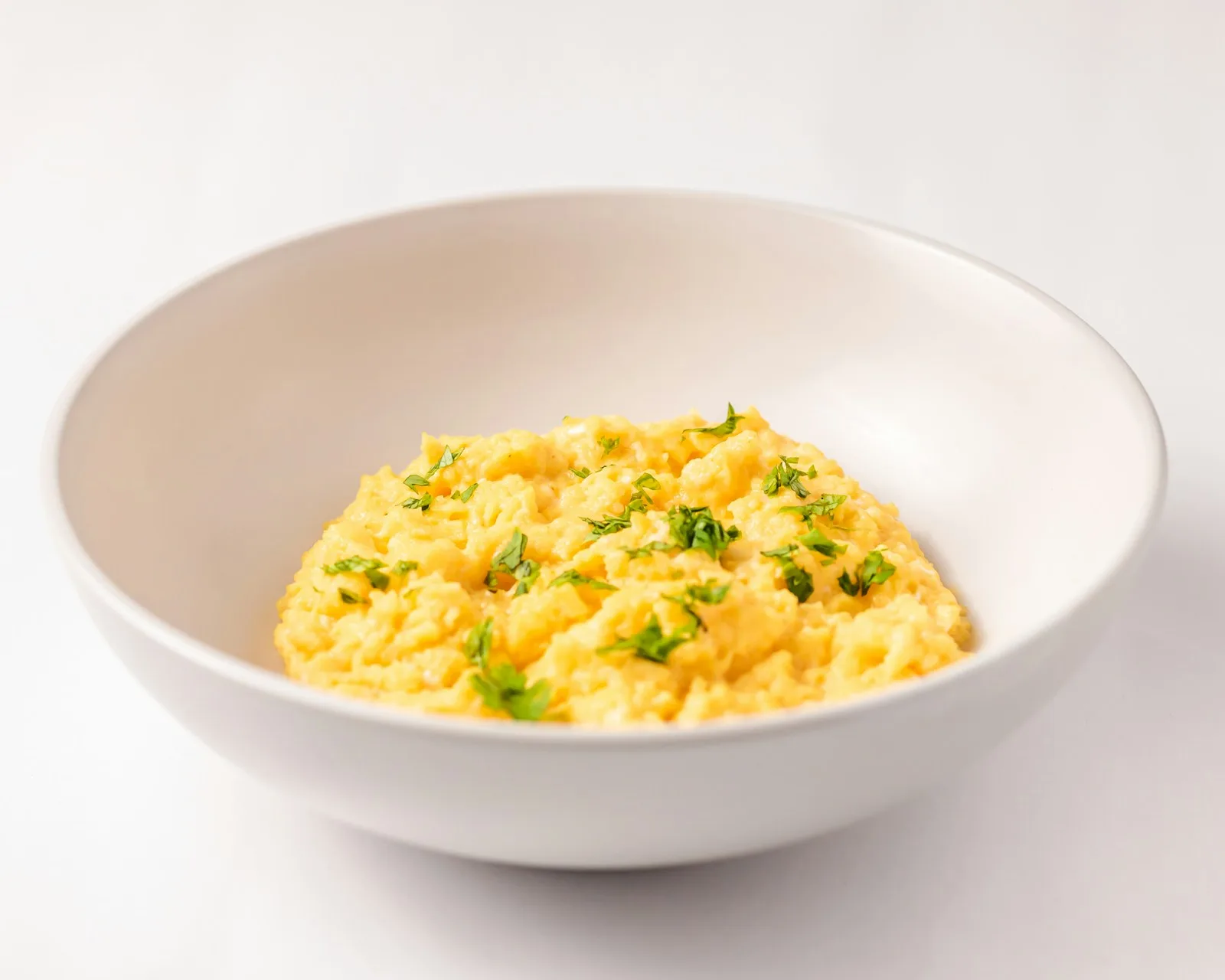 Soft, fluffy scrambled eggs topped with chopped herbs in a white bowl