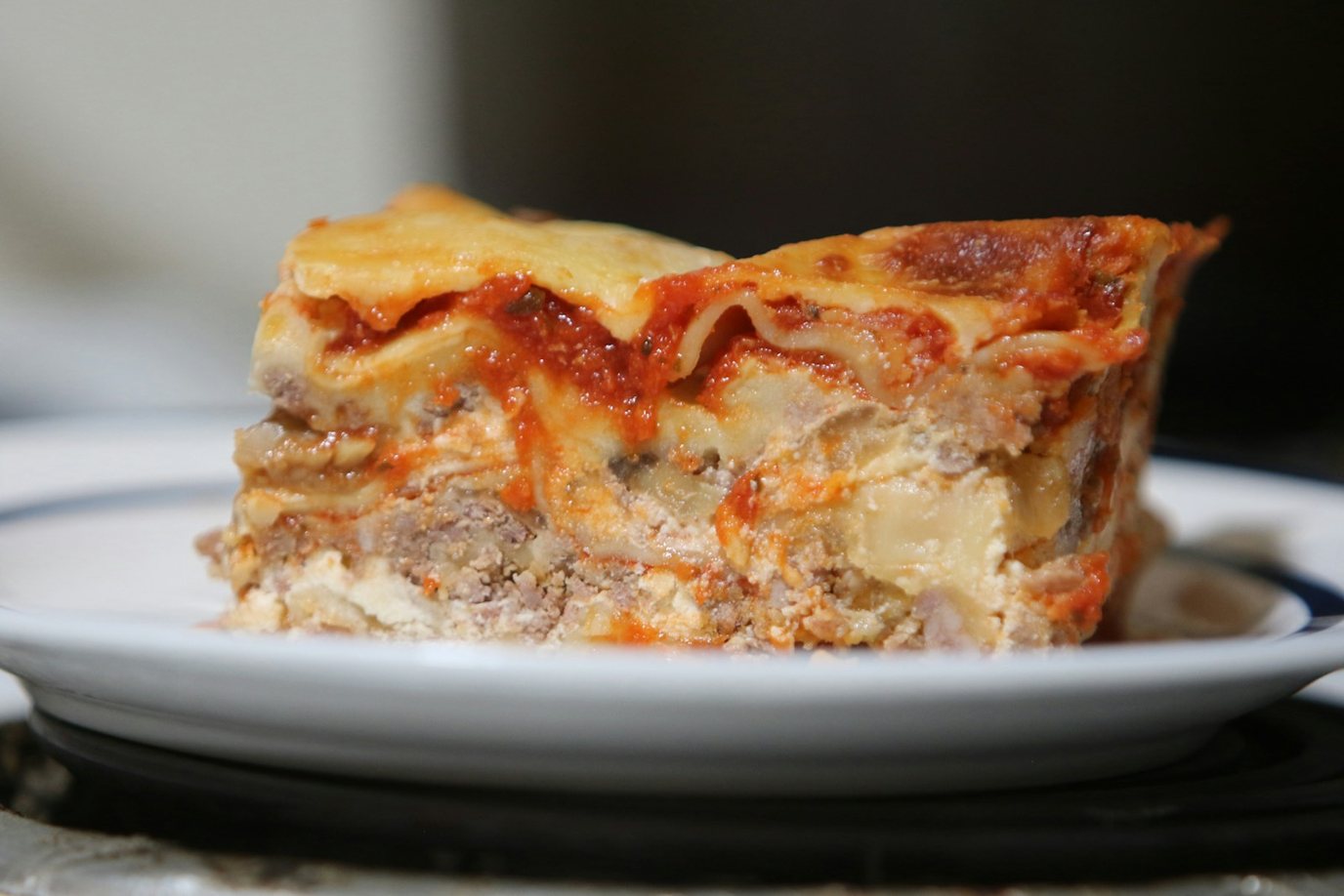 Cottage cheese lasagna slice on a white plate showing layers of noodles, ground beef sauce and a creamy cheese layer under browned mozzarella