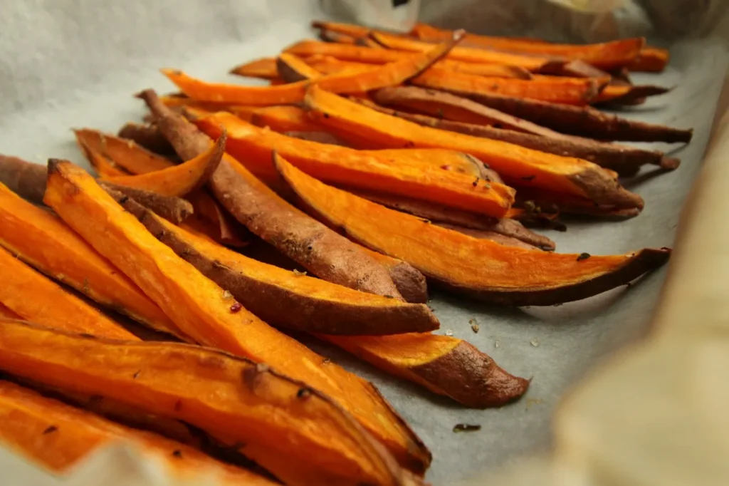 Golden sweet potato fries with skins on, spread on parchment paper